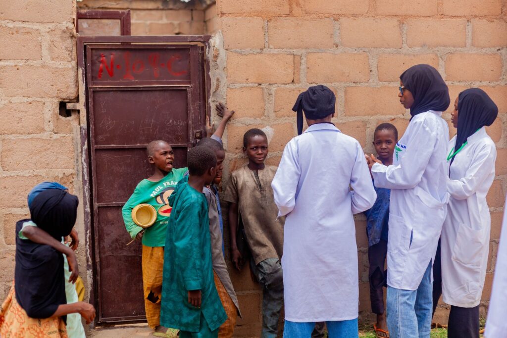 Health workers talk with village children during a community health visit in Gombe
