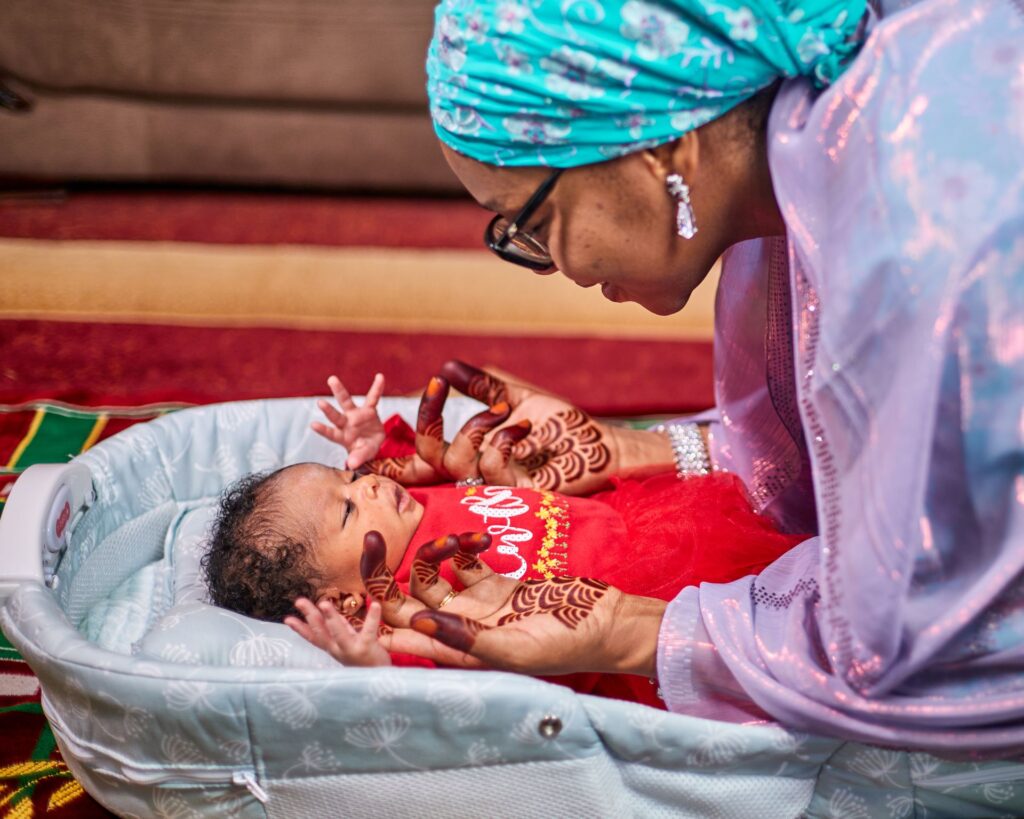 A mother in Kaduna holds her newborn baby close, her hands decorated with henna