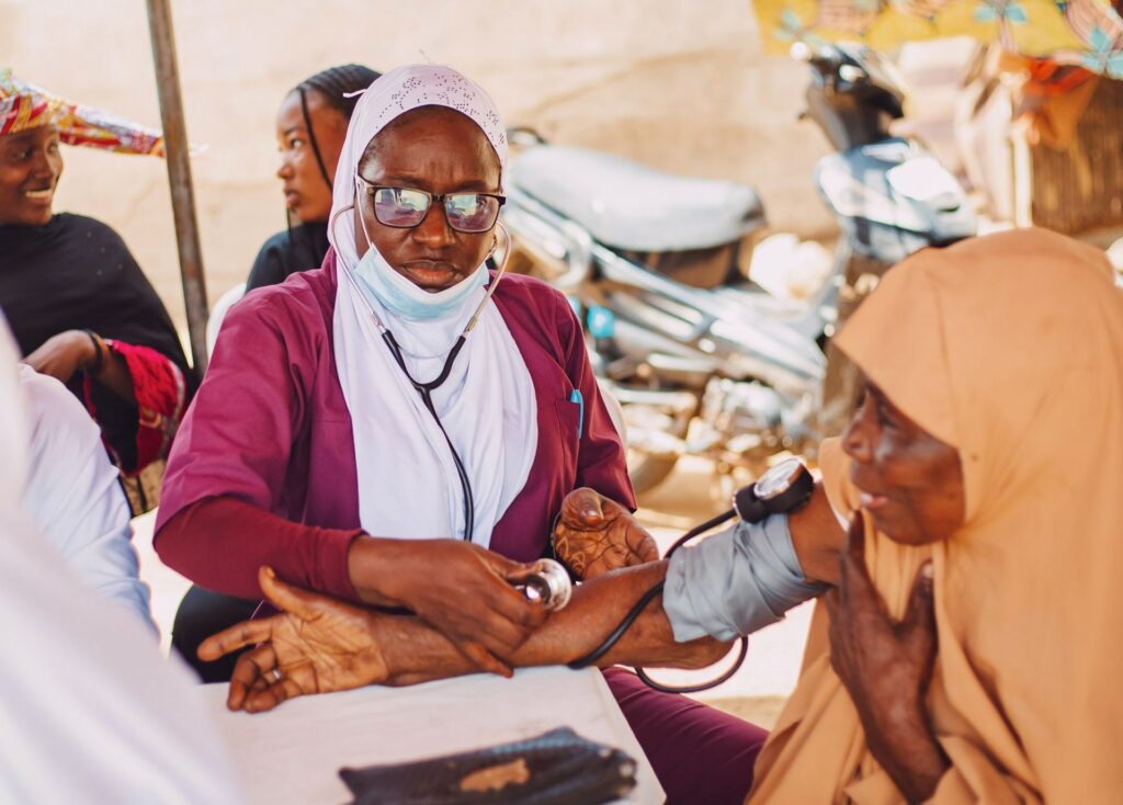 A health worker with a stethoscope examines a patient at an outdoor community clinic in Kaduna