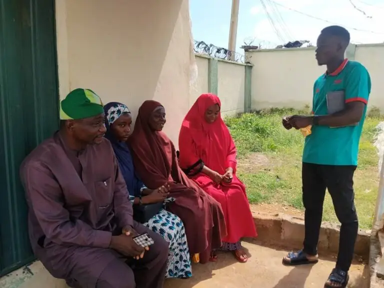 An LHAAT member standing and speaking to seated community members outside a facility in Igabi, Kaduna