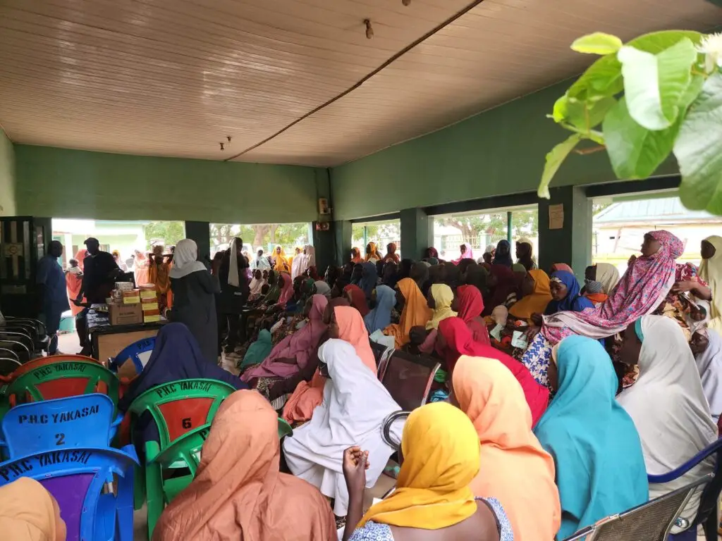 A large gathering of community members seated under a pavilion at PHC Yakasai in Soba, Kaduna